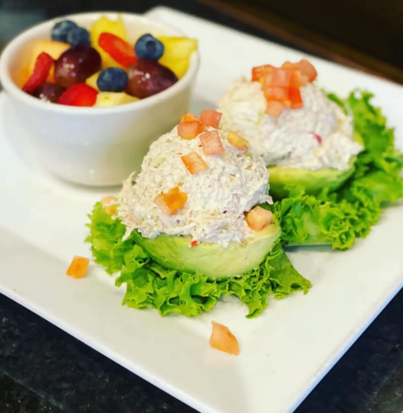 Two avocado halves filled with chicken salad and diced tomatoes, served with a fruit cup.