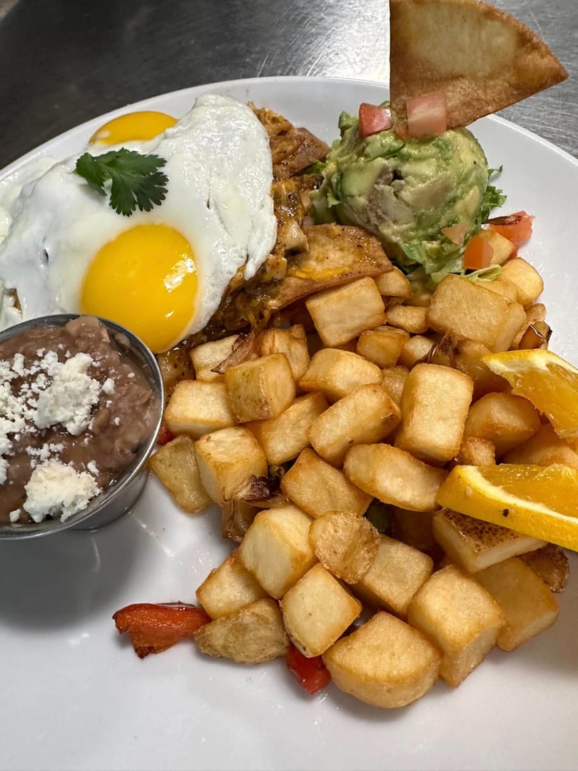 Breakfast plate with fried eggs, home fries, refried beans, guacamole, and a tortilla chip.