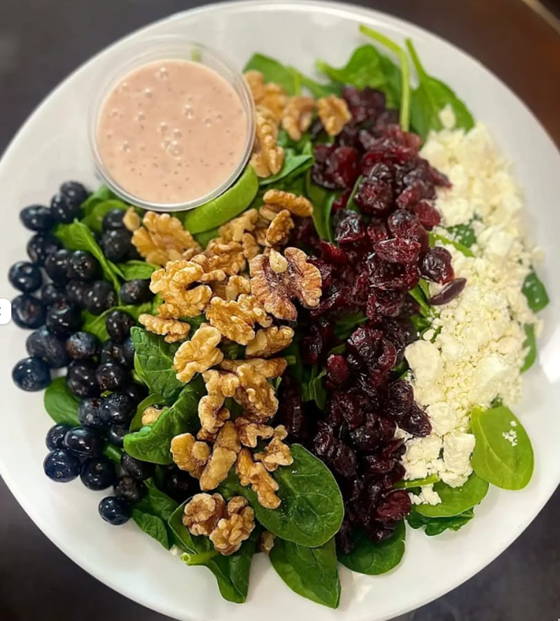 A vibrant spinach salad with blueberries, walnuts, dried cranberries, feta cheese, and dressing.