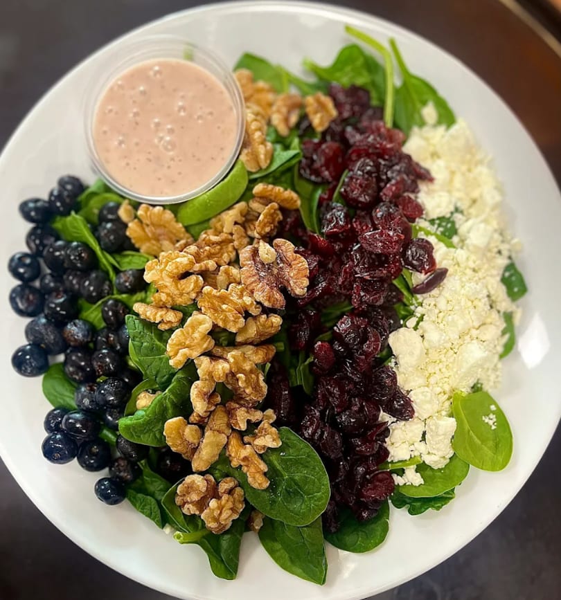 Spinach salad with blueberries, walnuts, dried cranberries, feta cheese, and a side of dressing.