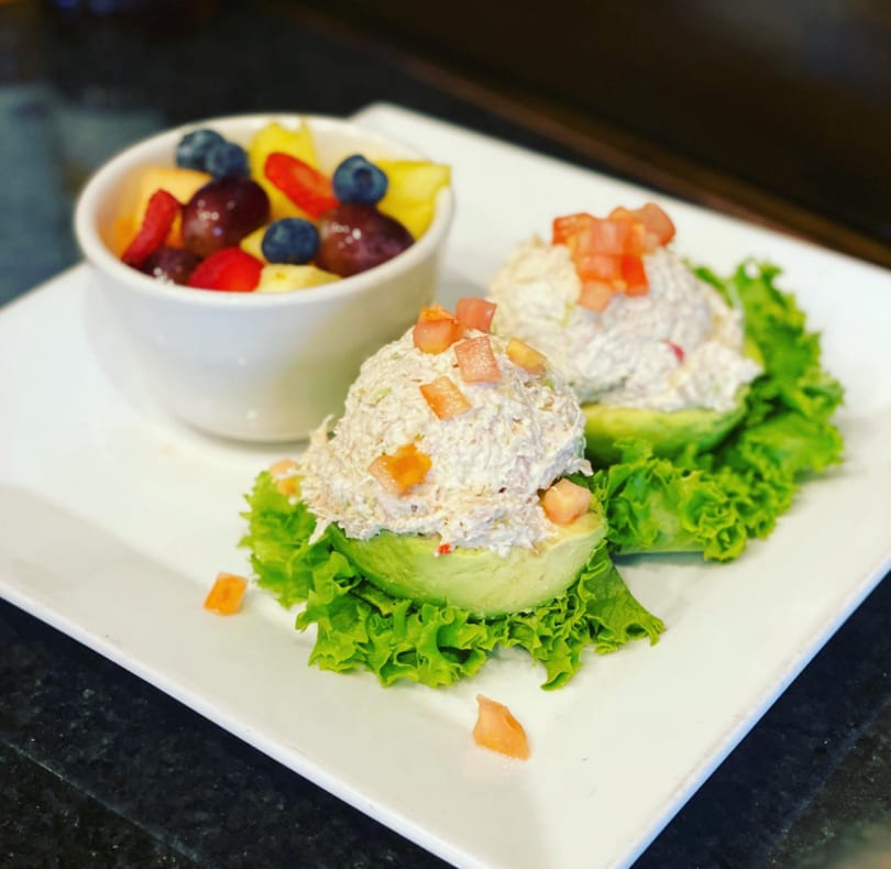 Two avocado halves filled with chicken salad and diced tomatoes, served with a fruit cup.